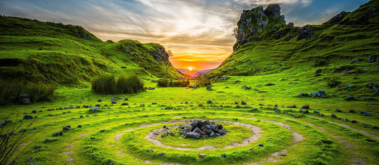 Circles of stones mark a grassy valley with a sunset in the background